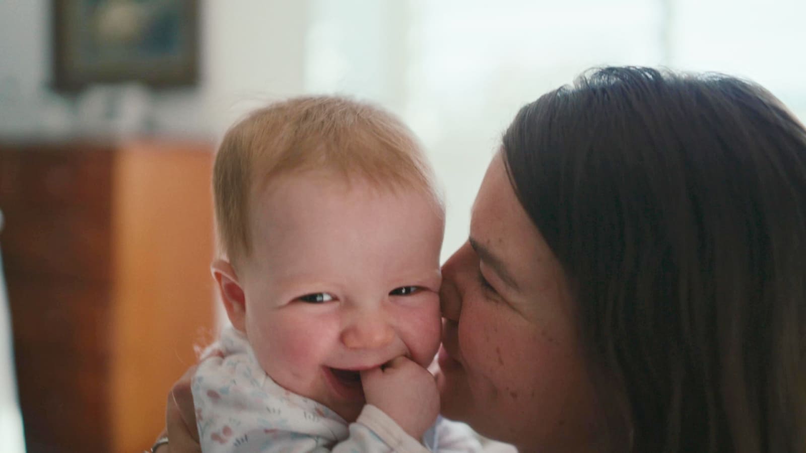 'A woman kissing a smiling baby.'