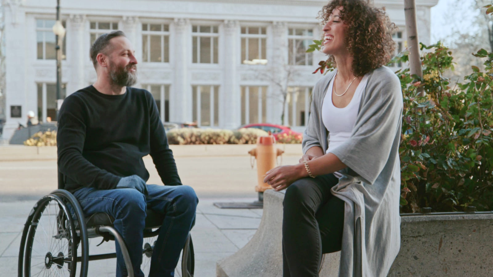 'A man in a wheelchair and a woman are smiling and talking are smiling and talking.'