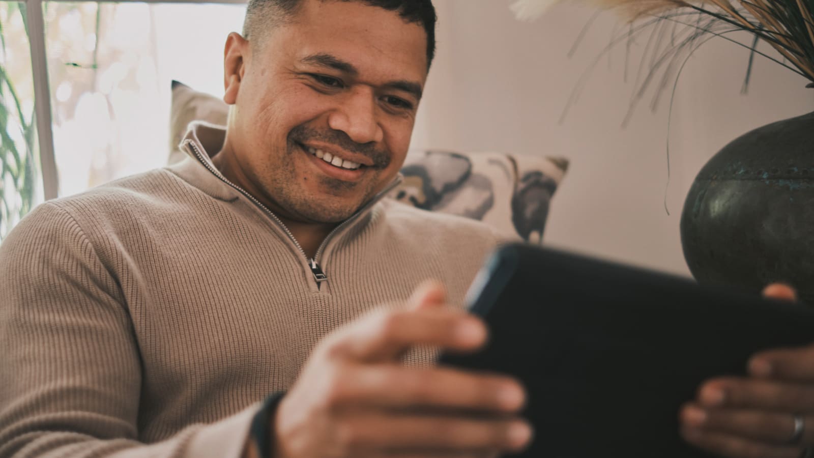 'A man smiling and looking at a tablet.'
